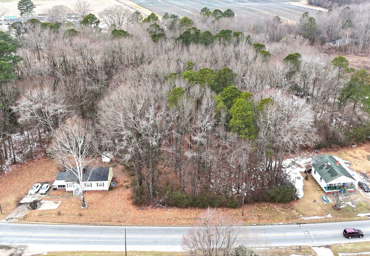 Aerial view of the wooded lot with a white house to the left and a green-roofed house to the right, road along the bottom.