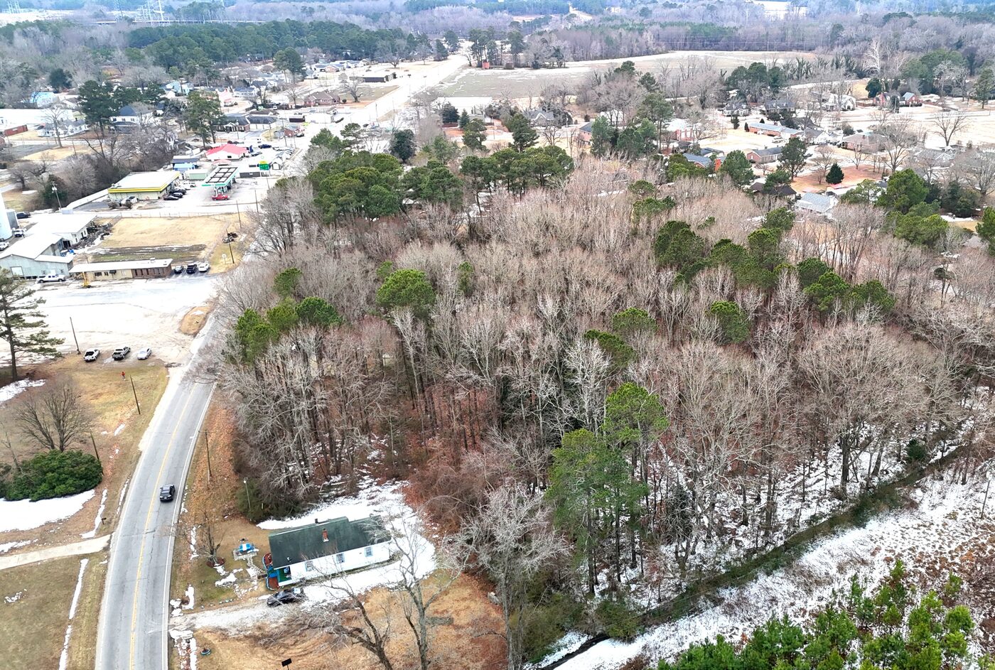 Wider drone view showing the lot within Battleboro, with the road curving past small commercial buildings.