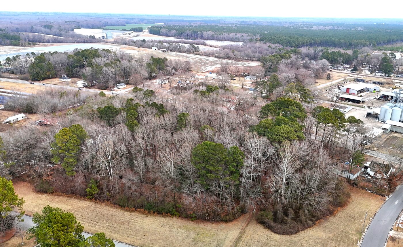 High drone view showing the surrounding farmland, solar arrays and scattered buildings around the village.