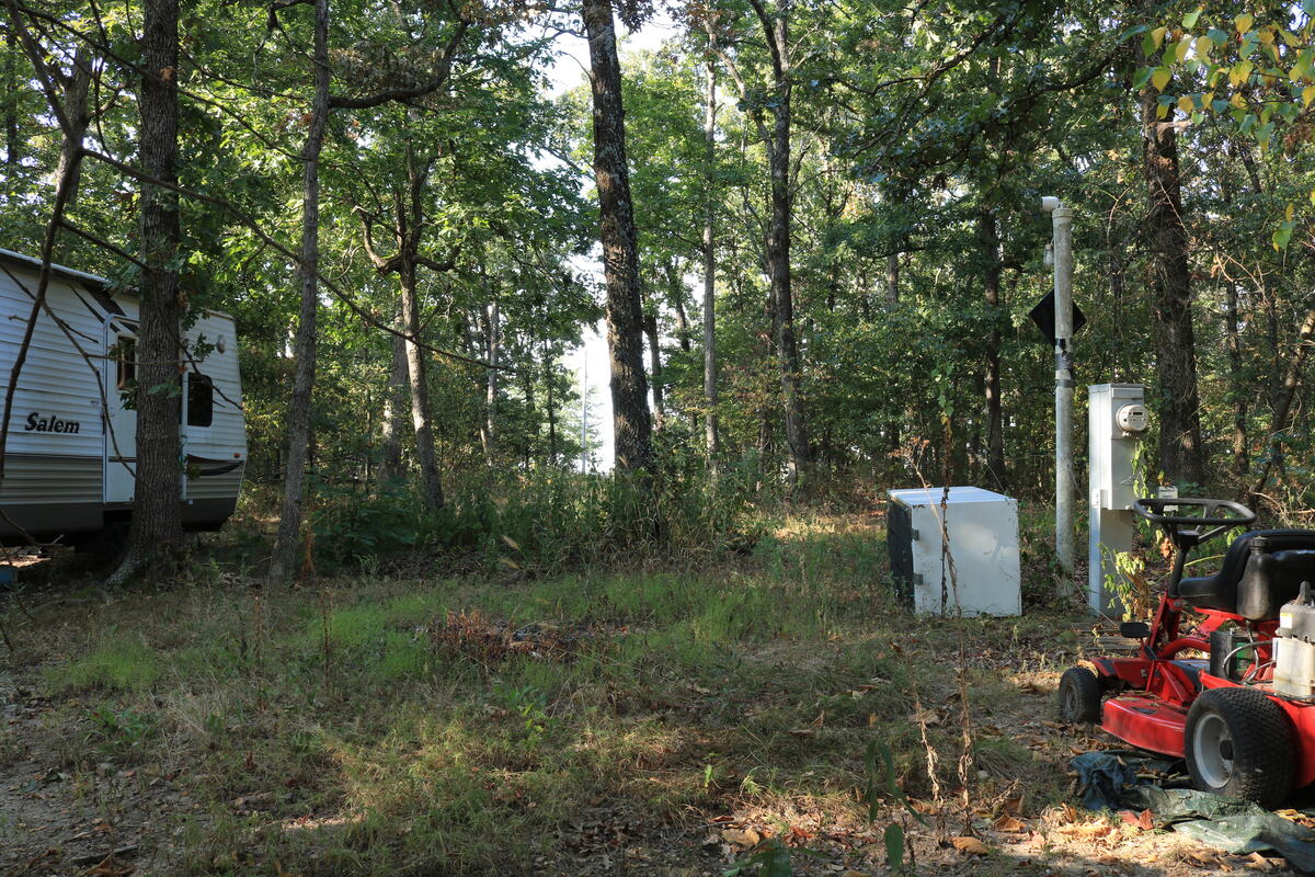 Cleared campsite with a travel trailer parked under the trees.