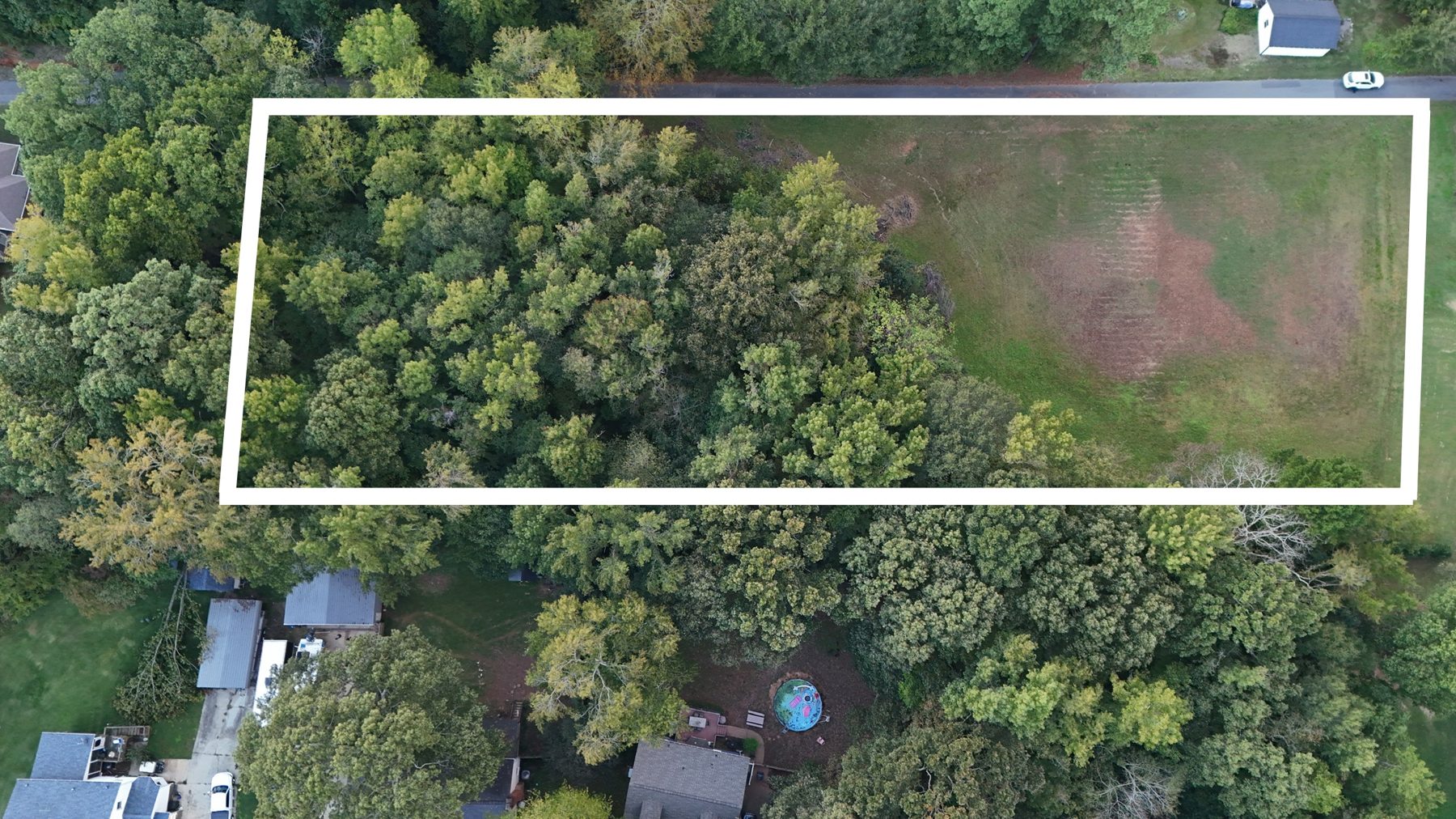 Drone view of the lot from the other side, the lane along the top, field on the right and woods on the left, boundary drawn in white.