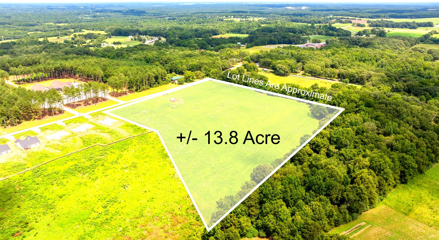 Drone view of the pasture outlined in white from the other side, woods along its back line and new homes beyond.